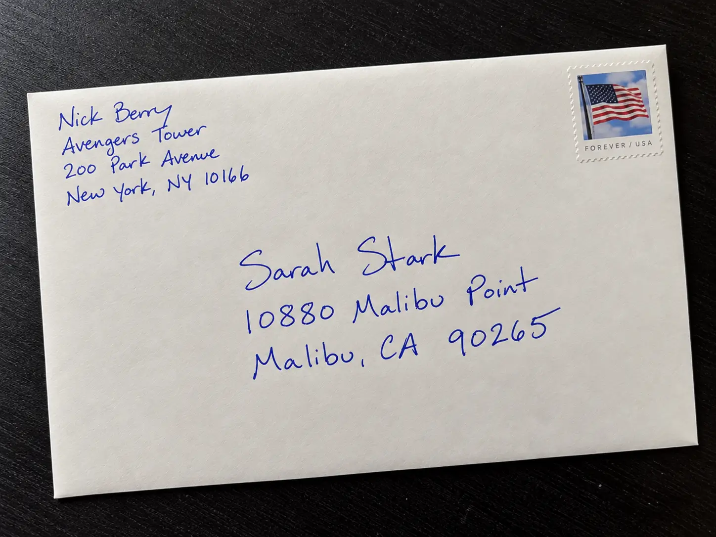 A matching envelope addressed by hand in blue ink, with a return address and an American flag First-Class postage stamp.